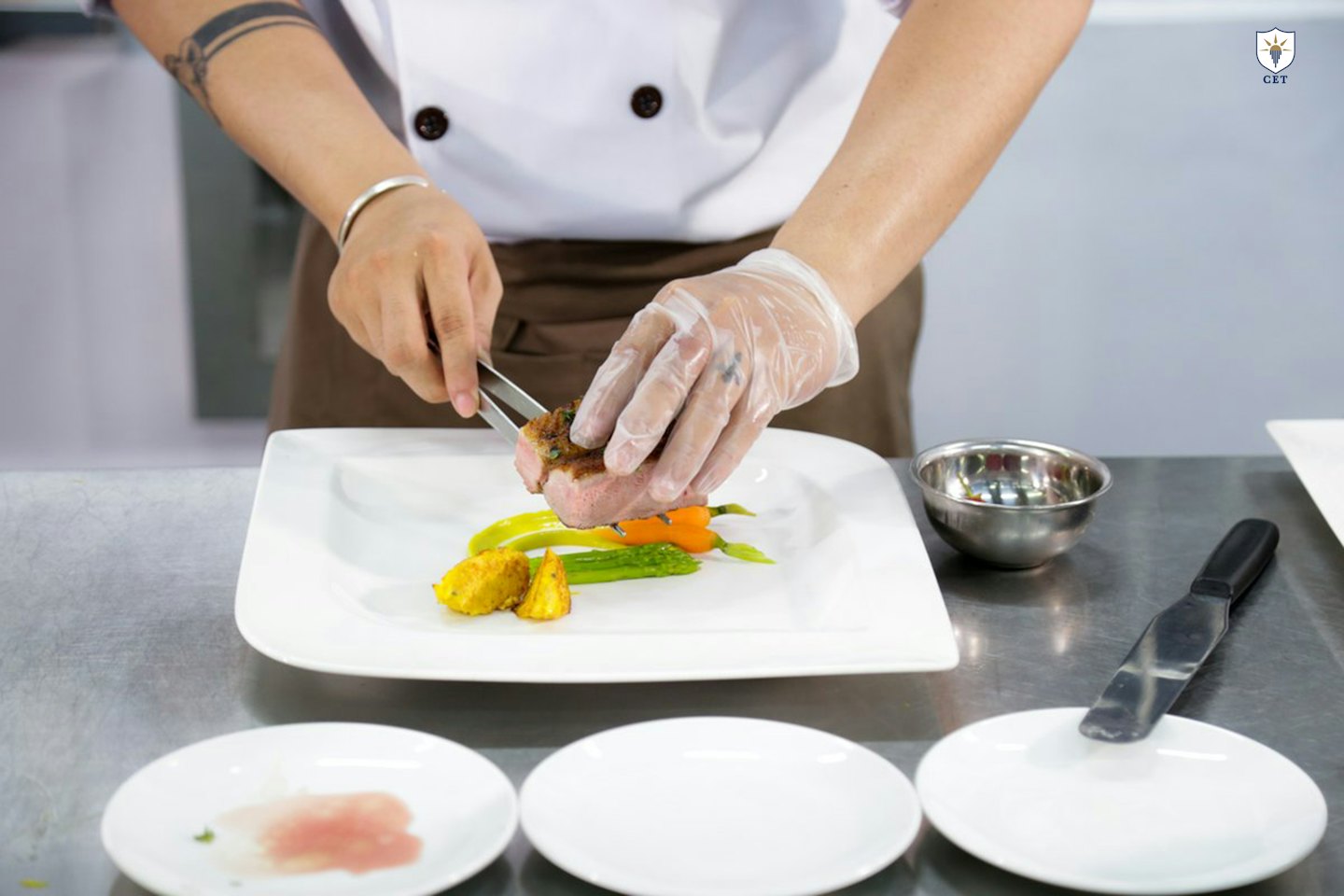 Chef carefully places roasted vegetables and meat onto a plate.