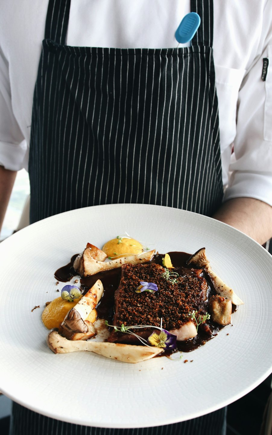 Chef presents a gourmet dish with mushrooms and edible flowers.