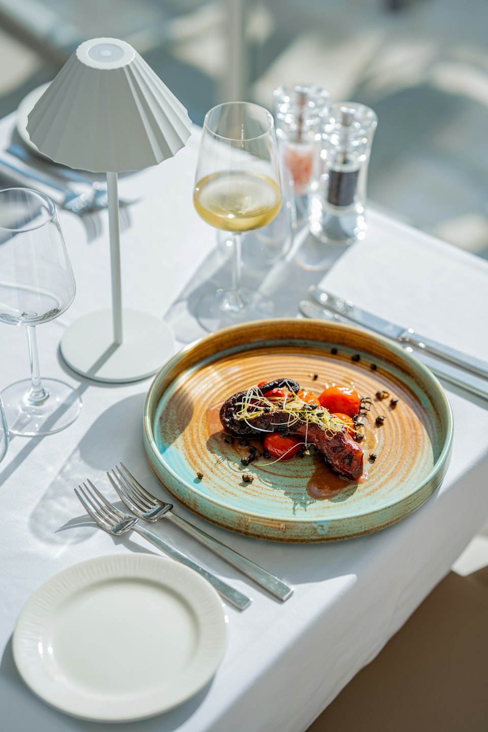 Gourmet lamb dish with roasted tomatoes and microgreens on a ceramic plate.